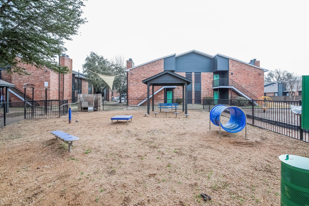 A playground with a blue slide and a green trash can.