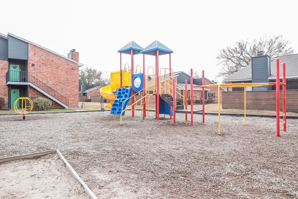 A playground with a blue and yellow slide and red poles.