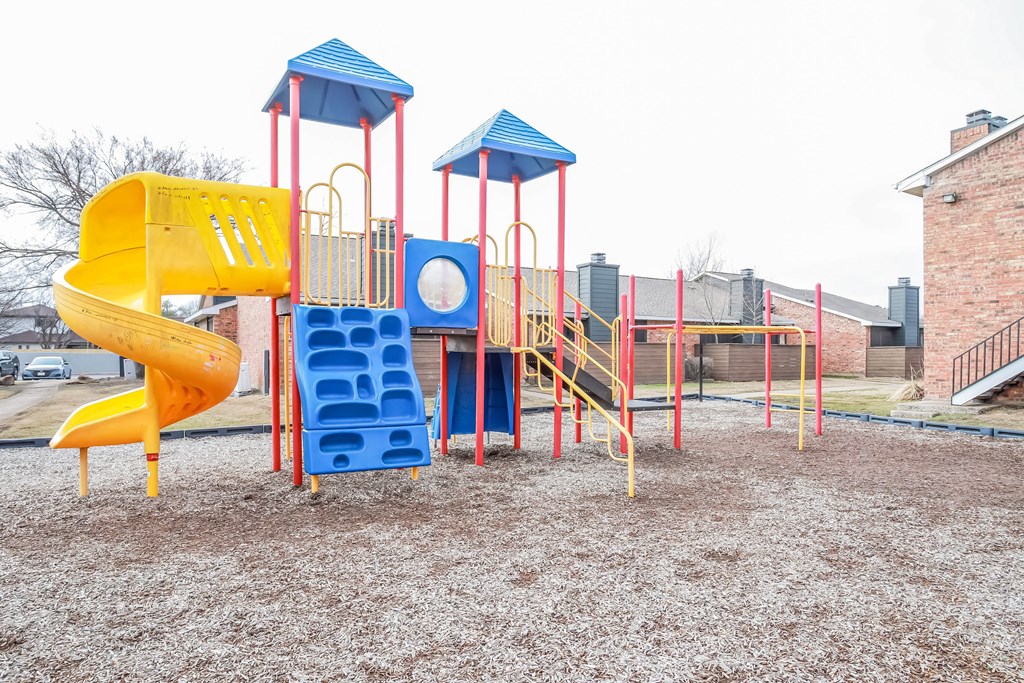 A playground with a yellow slide, blue and red climbing structures, and a red swing set.
