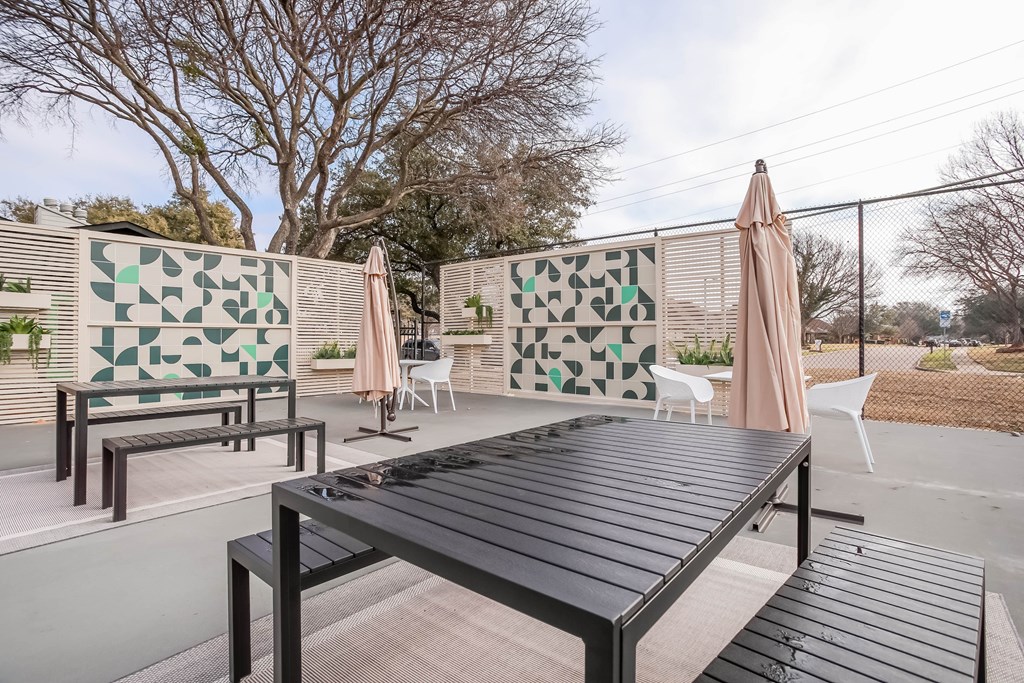 A black table is in the middle of a patio with a green and white tile wall behind it.