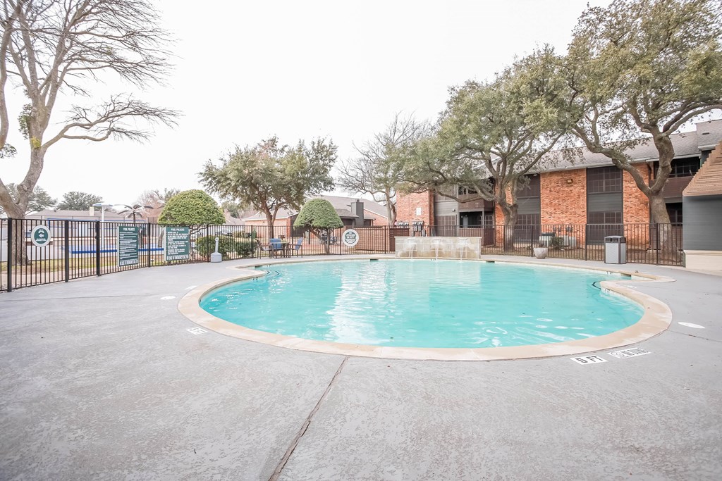 A small pool surrounded by a fence and trees.