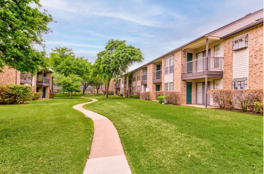 a walkway between two apartment buildings with grass and trees