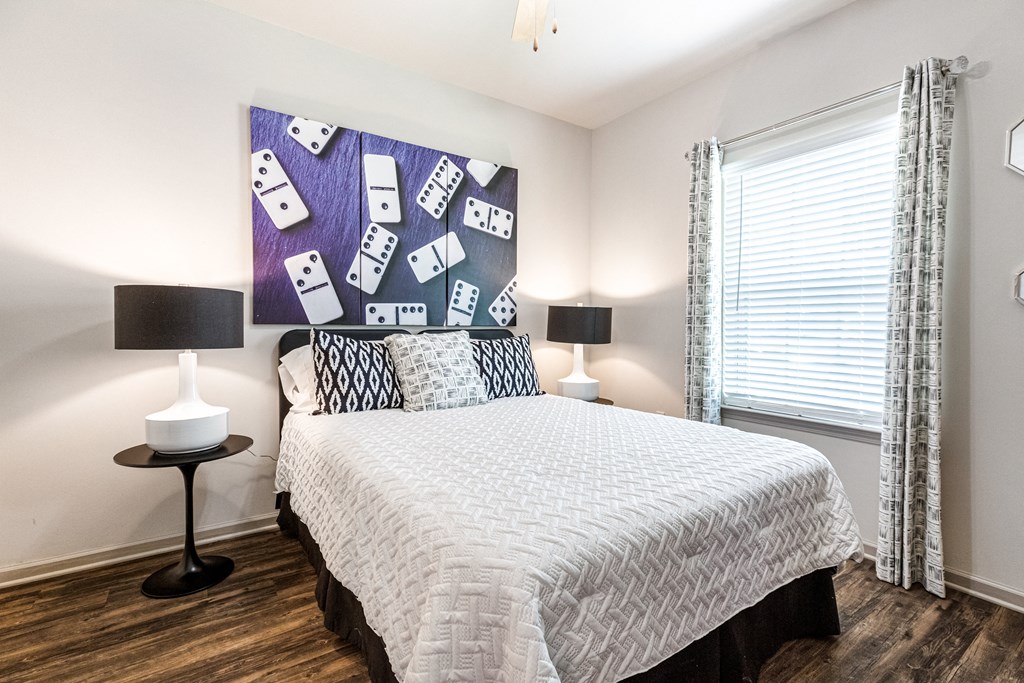 Furnished model bedroom with a window and wood-designed flooring at Reagan Crossing in Covington, LA