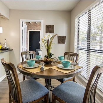 Model dining area with a circular table and 4 chairs in front of a large window at Forest Pointe Apartments in Macon, GA