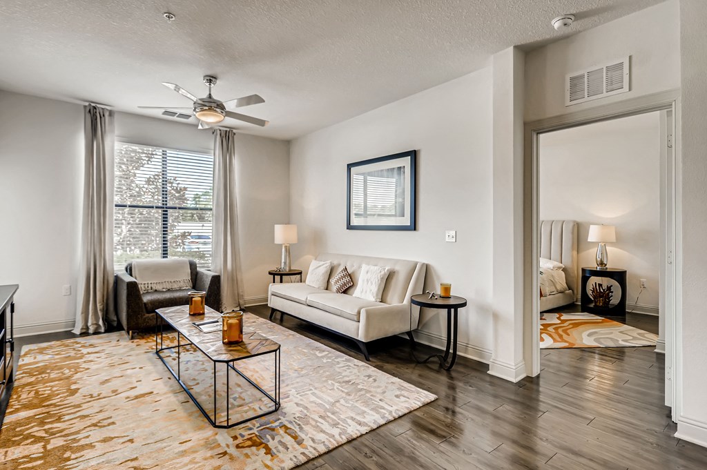 Model living room with wood-designed flooring and entry to bedroom at EOS in Orlando, FL