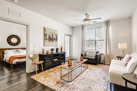 Model living room with wood-designed flooring, ceiling fan, and patio door at EOS in Orlando, FL