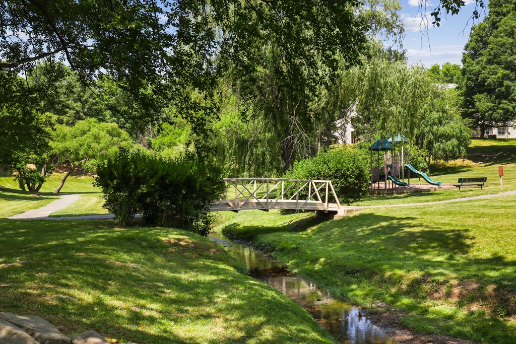 a small bridge over a stream with a playground in the background