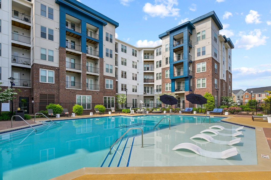 a swimming pool with chairs and umbrellas in front of an apartment building