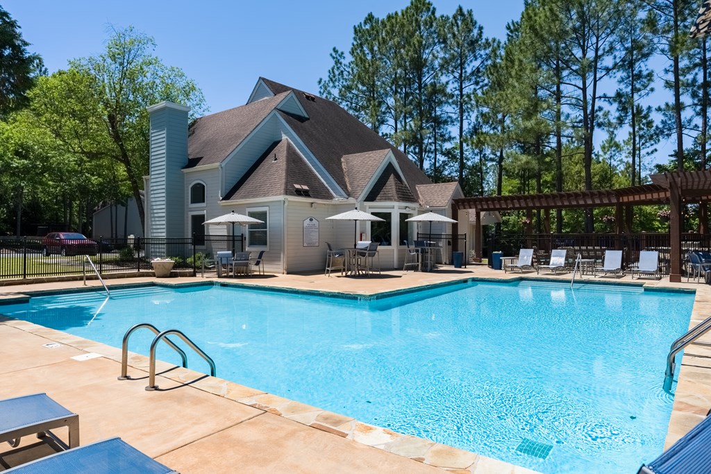 a swimming pool with lounge chairs and umbrellas in front of a house