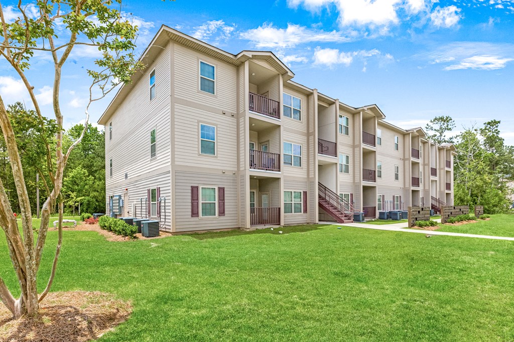 Three-story residential building with green lawn and trees at Reagan Crossing in Covington, LA