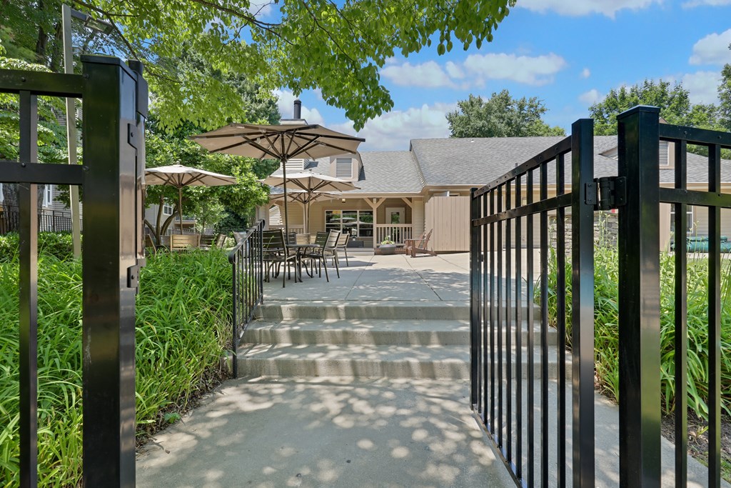 a gate leading to a patio with tables and umbrellas
