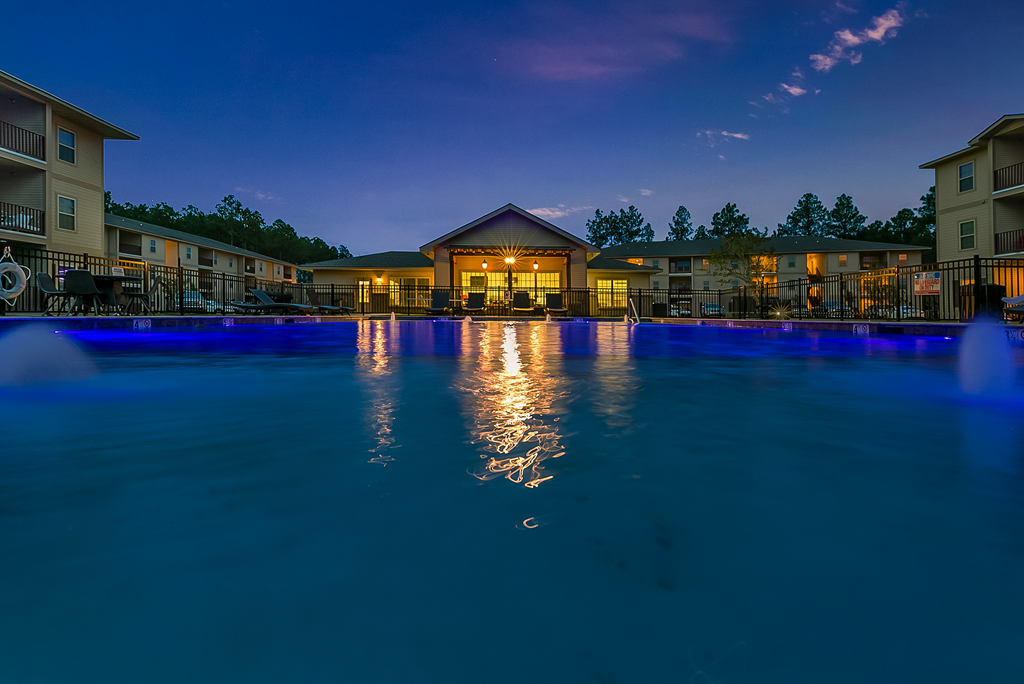 Outdoor swimming pool and clubhouse at night at Reagan Crossing apartments for rent in Covington, LA