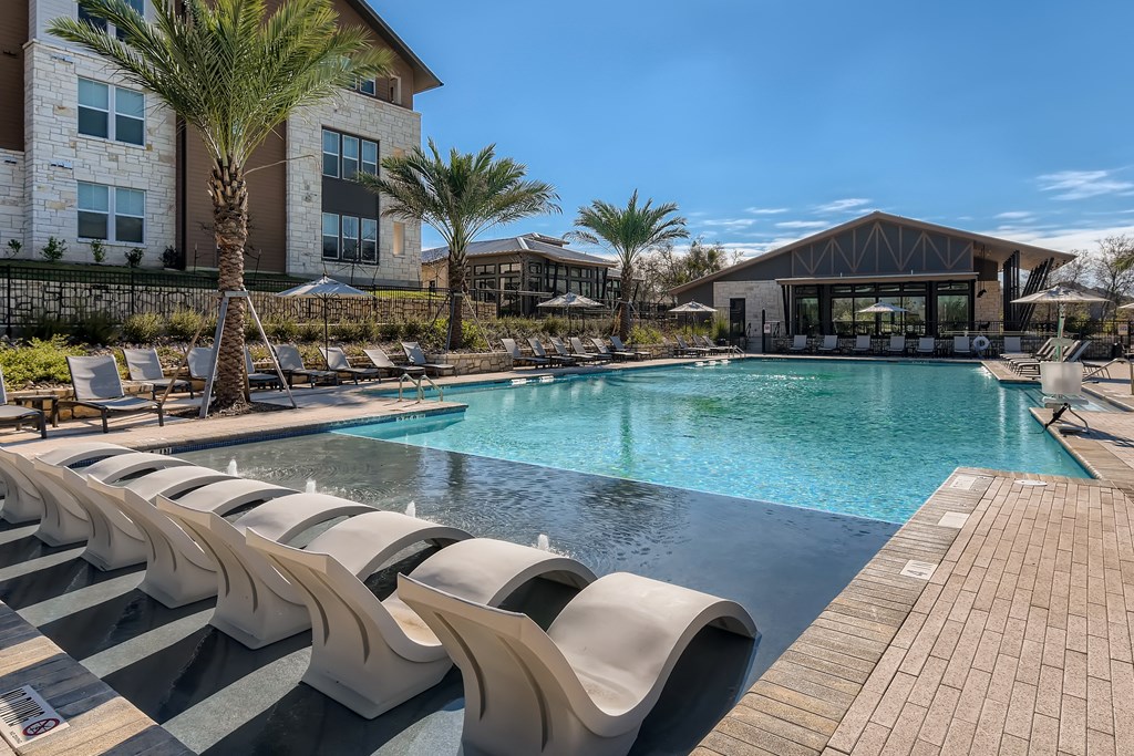 Resort-style swimming pool with in-water lounge chairs overlooking the clubhouse at Cypress McKinney Falls in Austin, TX