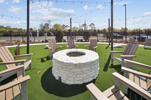 A white fire pit sits in the middle of a grassy area surrounded by wooden chairs. at Allegra at Cocoa in Cocoa, FL, 32926