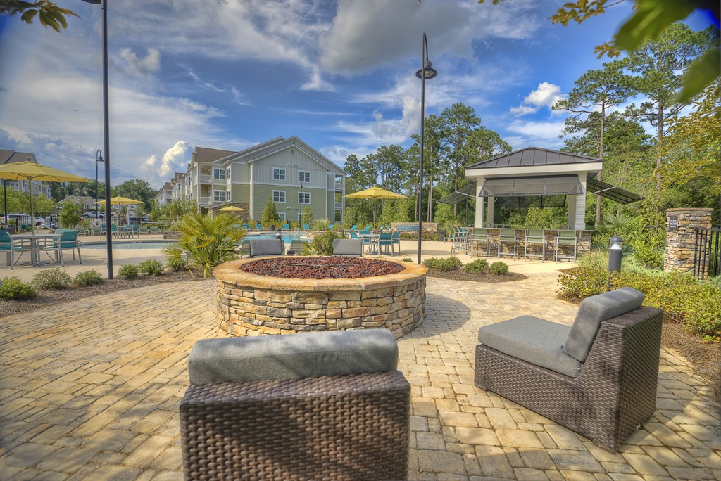 Poolside fire pit with oversized chairs, outdoor grilling station, and tables at Lullwater at Blair Stone apartments for rent in Tallahassee, FL