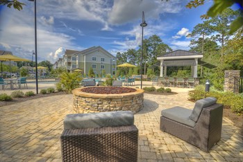 Poolside fire pit with oversized chairs, outdoor grilling station, and tables at Lullwater at Blair Stone apartments for rent in Tallahassee, FL - Photo Gallery 5