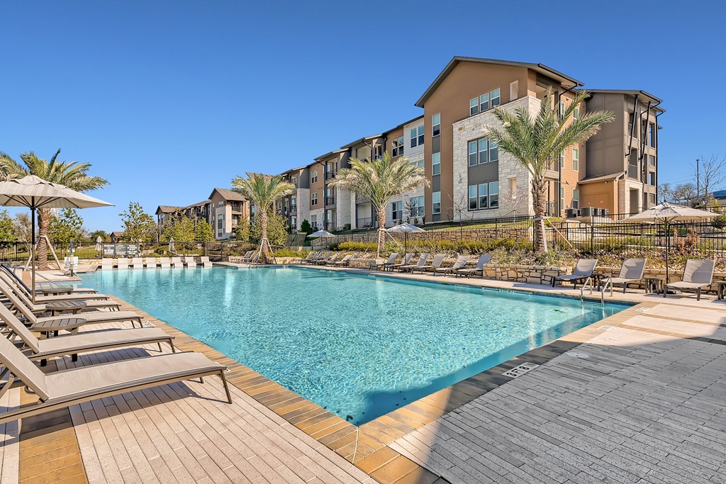 Resort-style swimming pool surrounded by sundeck with lounge chairs and umbrellas at Cypress McKinney Falls in Austin, TX