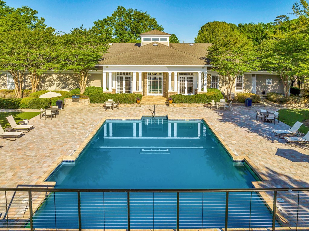 a backyard with a pool and patio with lounge chairs and a house in the background