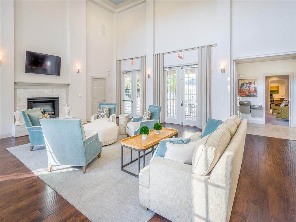 Interior of the clubhouse with ample seating, an ottoman, tables, high windows, high ceiling, and access to outside at Evergreens at Mahan apartments  in Tallahassee, FL