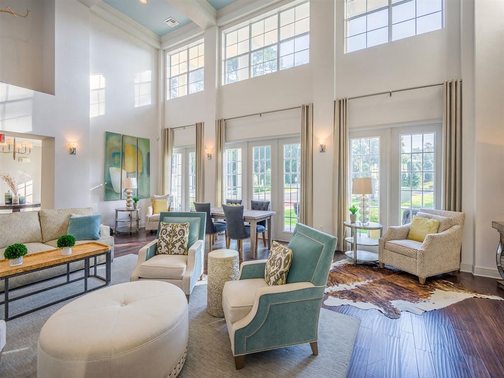 Tallahassee, FL apartment complex resident clubhouse with plush chairs, wood-designed flooring, and high ceiling at Evergreens at Mahan