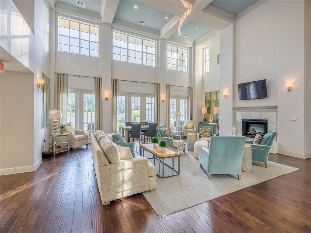 Interior of clubhouse with plush chairs, an ottoman, tables, on-wall TV, wood flooring and high ceiling at Evergreens at Mahan