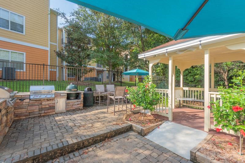 Tallahassee FL apartment complex grilling pavilion with two grills, lounge chairs, brick flooring, and a roofed sitting area at Evergreens at Mahan