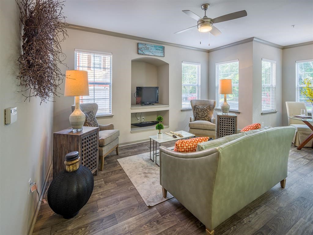 Furnished living room with sofas, two nightstands, numerous windows, wood-designed flooring, and high ceiling at Evergreens at Mahan apartments in Tallahassee, FL