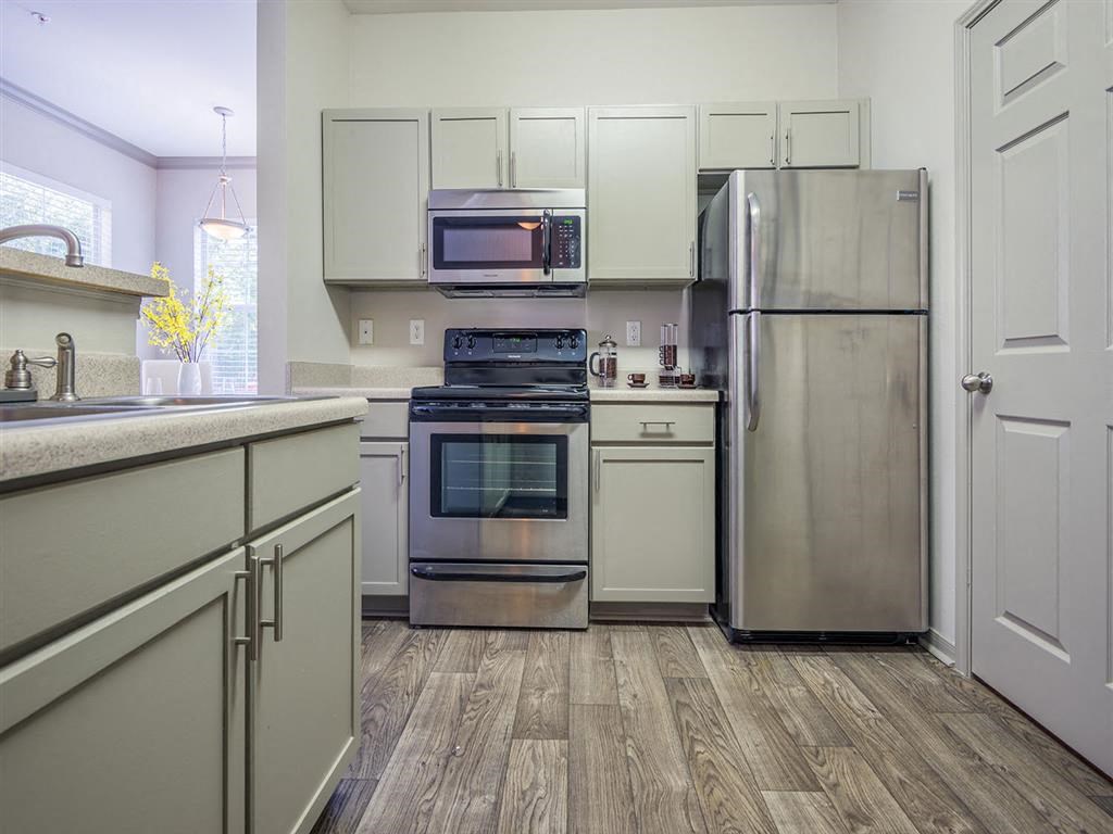 Tallahassee FL apartment kitchen area with stainless steel appliances, shaker-style cabinetry, and wood-designed flooring at Evergreens at Mahan