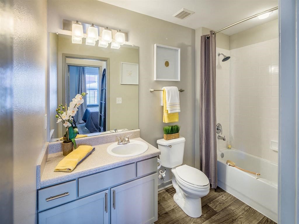 Bathroom with tub/shower, toilet, and sink with extended counter, wood designed flooring and high ceiling at Evergreens at Mahan apartments in Tallahassee, FL