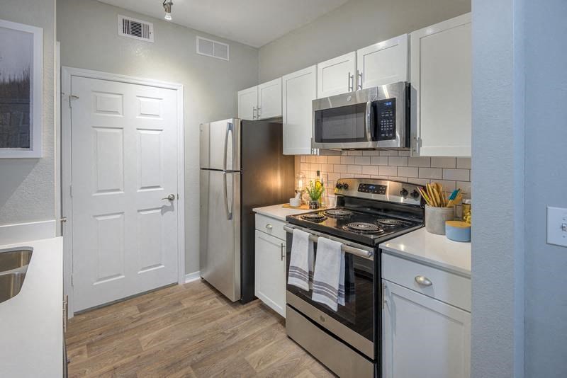 Tallahassee FL apartment kitchen area with stainless steel appliances, shaker-style cabinetry, and wood-designed flooring at Evergreens at Mahan