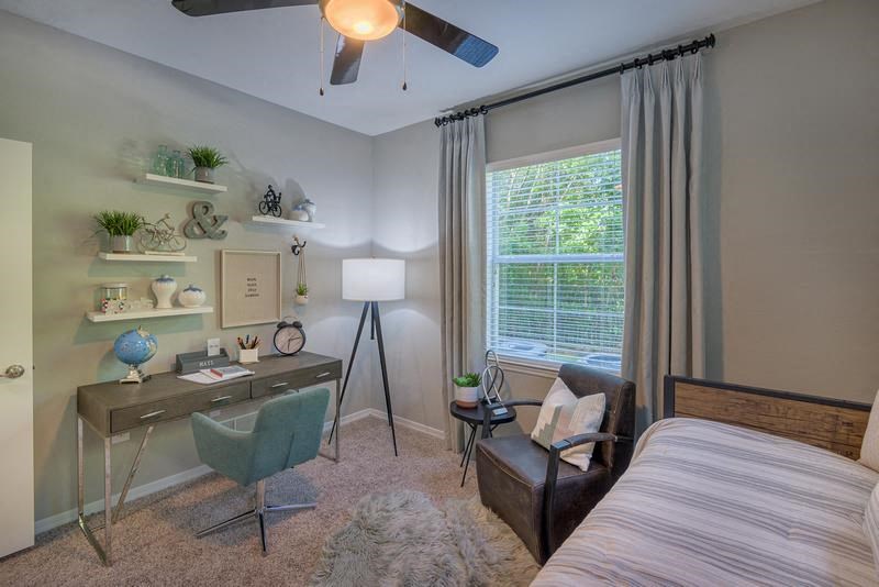 Guest bedroom and office with a window, ceiling fan, large windows, high ceiling, and carpeted flooring at Evergreens at Mahan apartments in Tallahassee, FL
