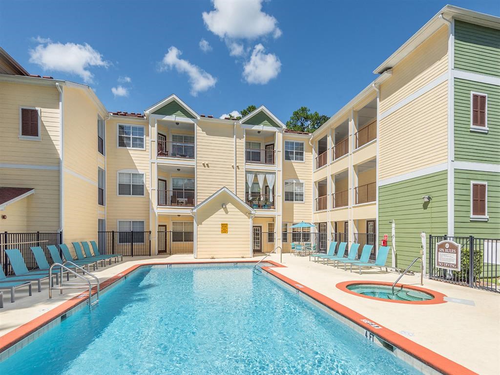 Sparkling resort-style swimming pool and hot tub with lounge chairs at Evergreens at Mahan apartments in Tallahassee, FL