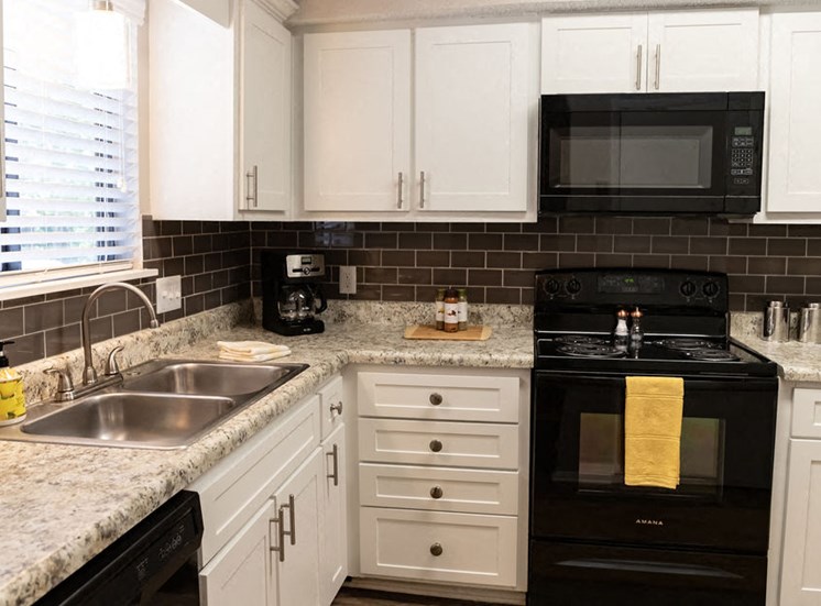 apartment kitchen with white cabinets black stove and microwave