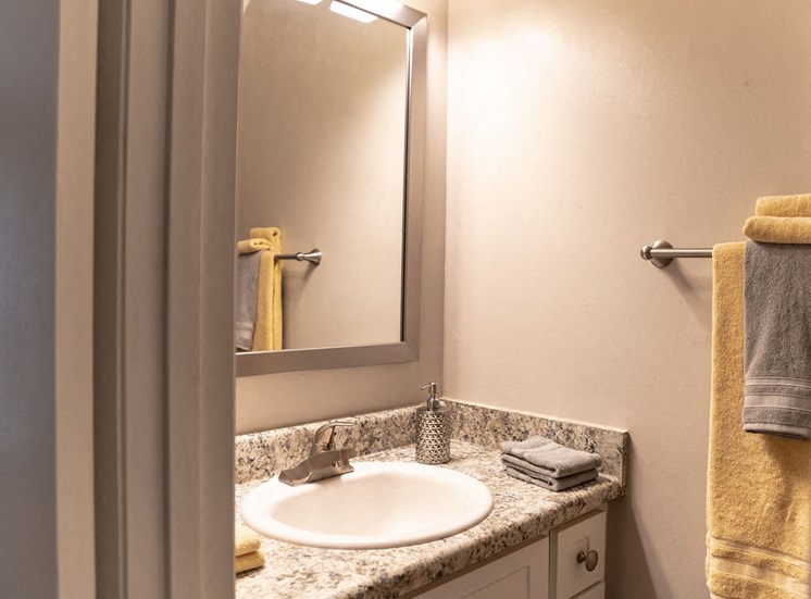 close view of apartment bathroom with sink mirror and yellow towels