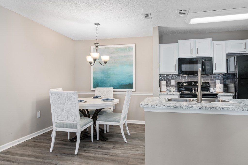 a dining area with a table and chairs and a kitchen in the background
