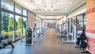 a spacious fitness center with weights and cardio equipment in a building with large windows