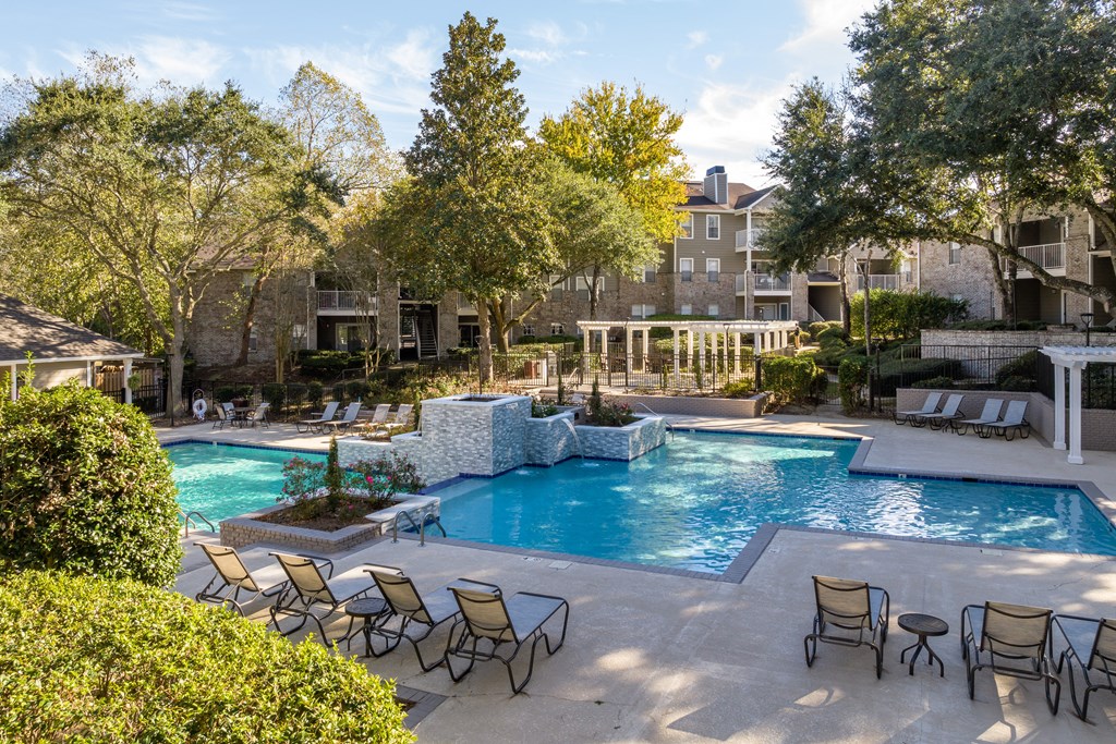 a swimming pool with chairs and trees and a building in the background