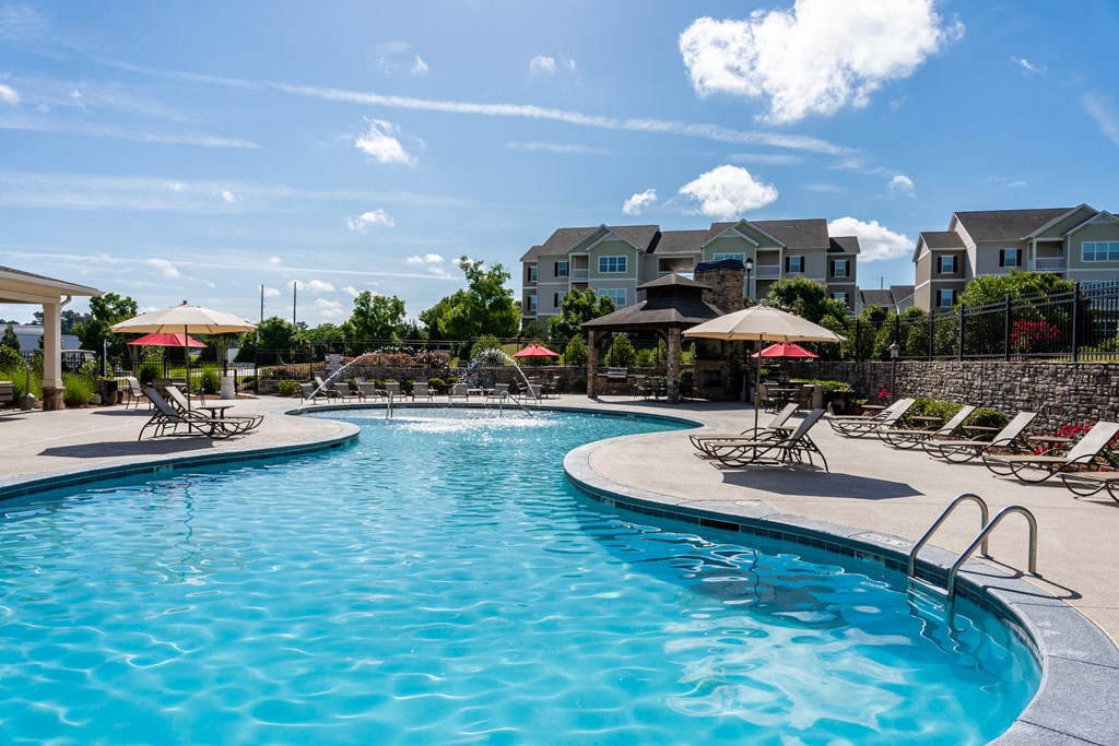 Resort-style swimming pool surrounded by lounge chairs, umbrellas, and pavilion at Riverstone apartments for rent in Macon, GA