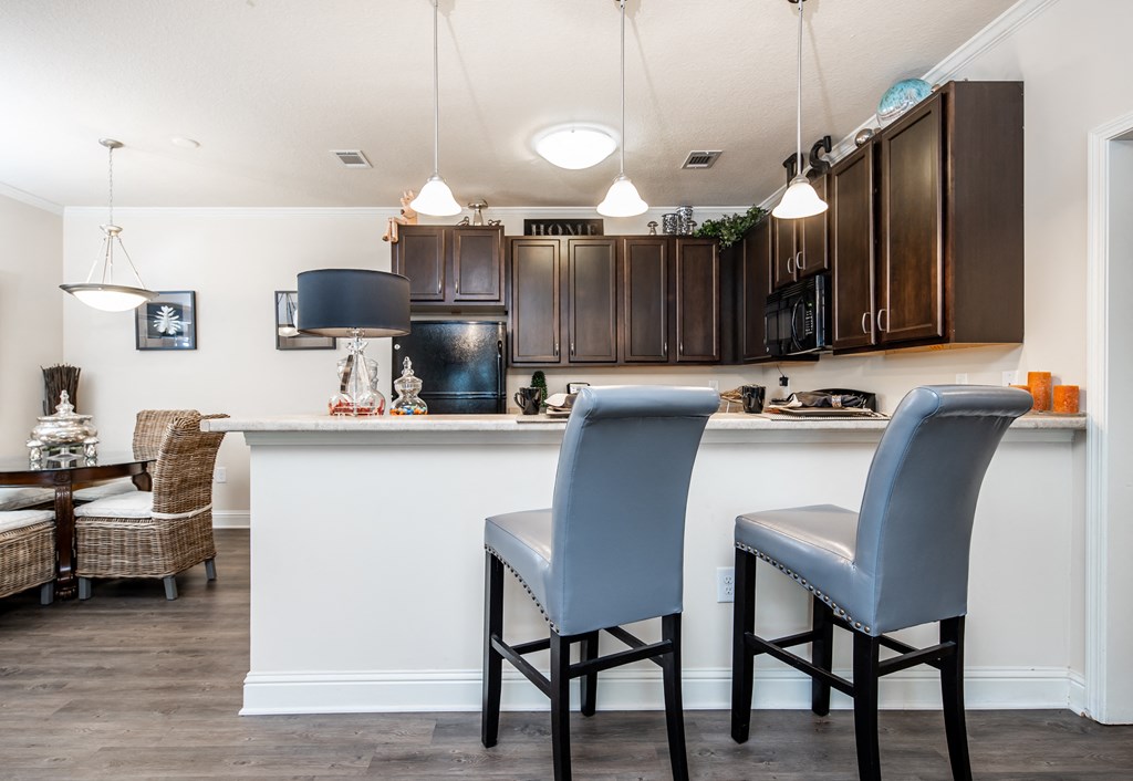 Kitchen bar counter with two bar chairs and dining area at Riverstone apartments for rent in Macon, GA