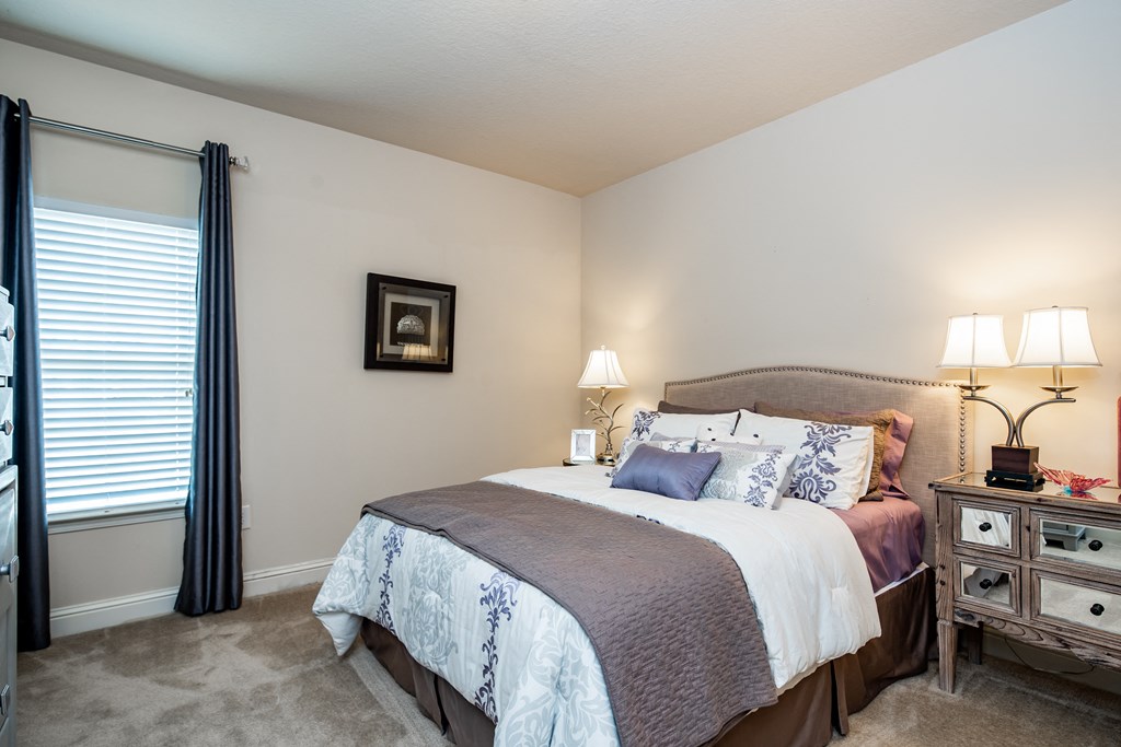 Furnished bedroom with beige walls, window, and carpet flooring at Riverstone apartments for rent in Macon, GA
