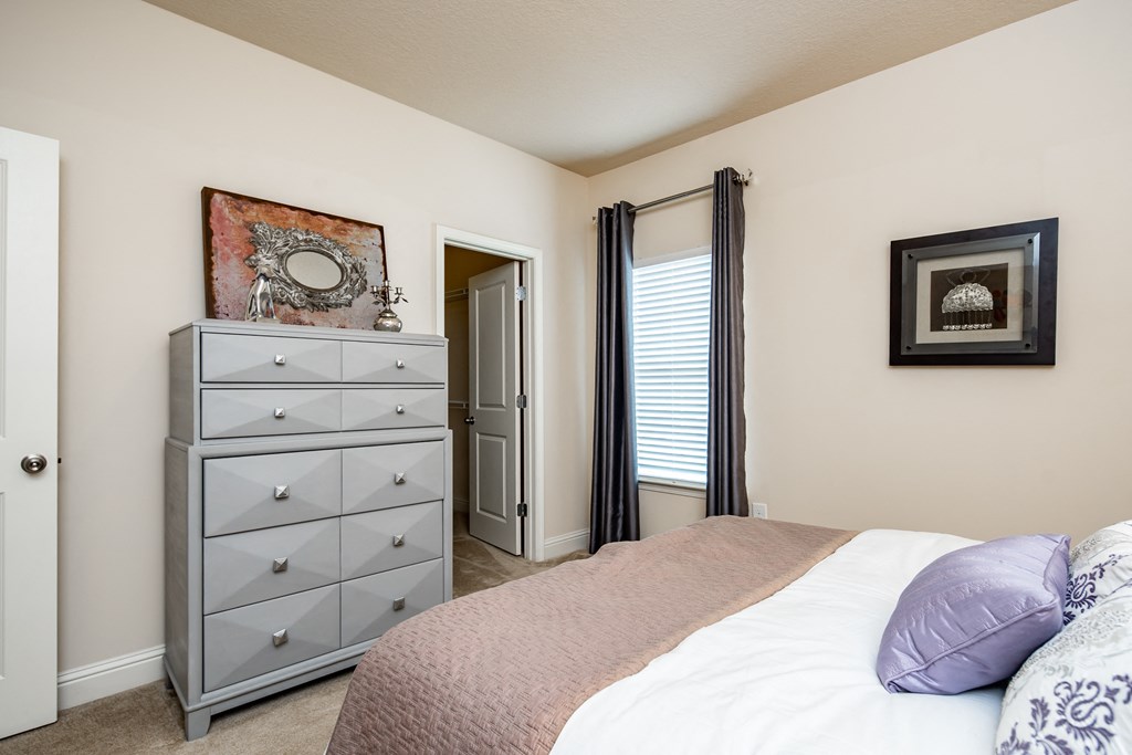 Furnished bedroom with beige walls, window, and carpet flooring at Riverstone apartments for rent in Macon, GA