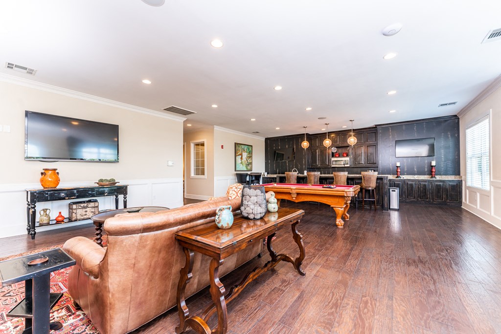 Clubhouse lounge with sofa and TV, pool table, and communal kitchen with bar counter at Riverstone apartments for rent in Macon, GA