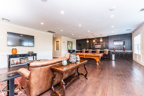 Clubhouse lounge with sofa and TV, pool table, and communal kitchen with bar counter at Riverstone apartments for rent in Macon, GA
