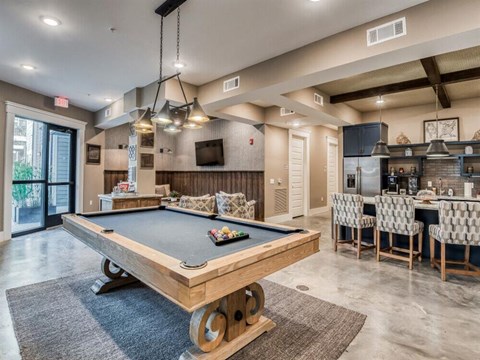 a pool table is in the center of a clubhouse with a bar and a kitchen
