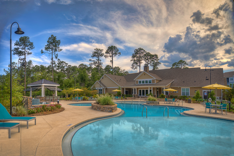 Resort-style swimming pool with lounge chairs with view of the resident clubhouse at Lullwater at Blair Stone apartments for rent in Tallahassee, FL