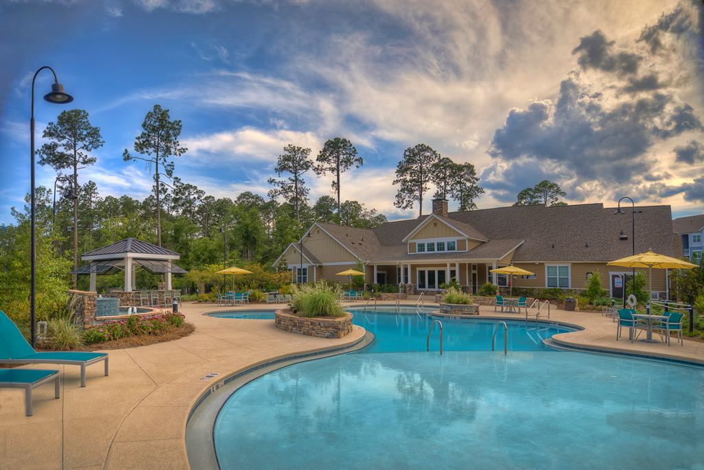 Resort-style swimming pool with lounge chairs with view of the resident clubhouse at Lullwater at Blair Stone apartments for rent in Tallahassee, FL