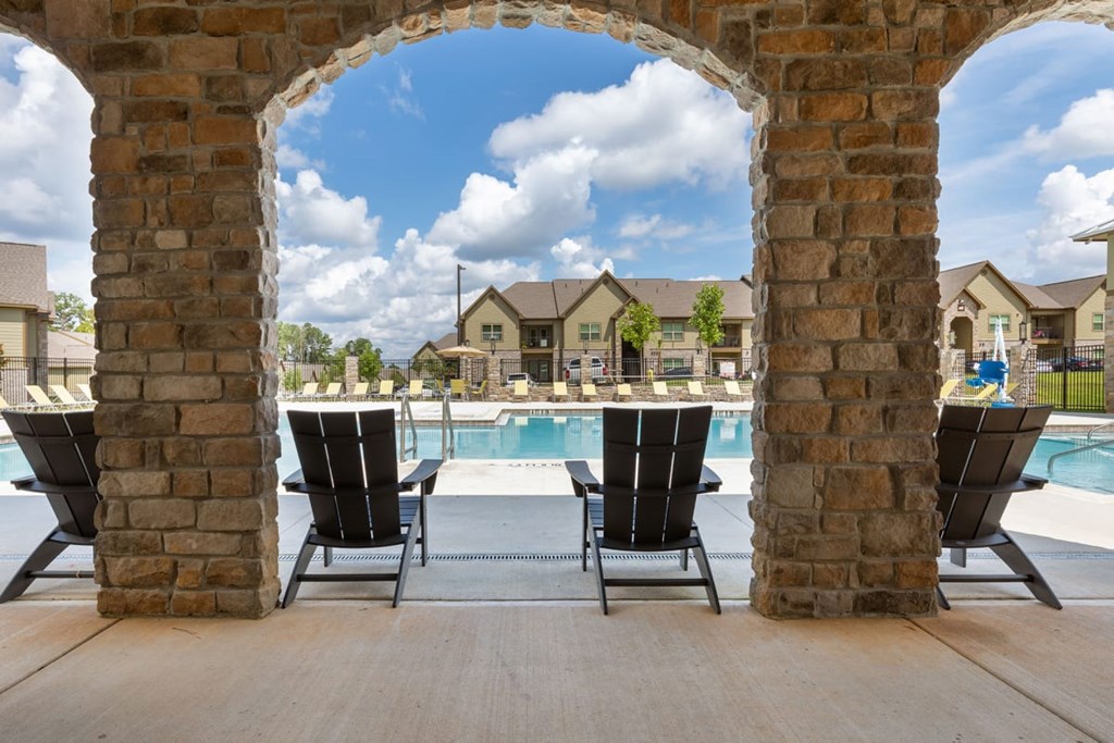 A view of a pool through an archway with chairs on the deck.