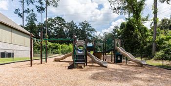 A playground with a green slide and a brown sandy area.