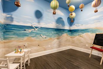 A room with a beach mural on the wall and hot air balloons floating above.