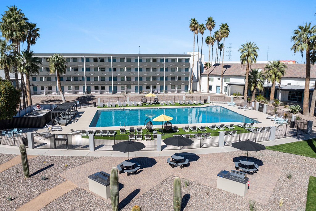 A pool surrounded by chairs and umbrellas with a building in the background at Presidio Palms Apartments, Tucson, AZ, 85701